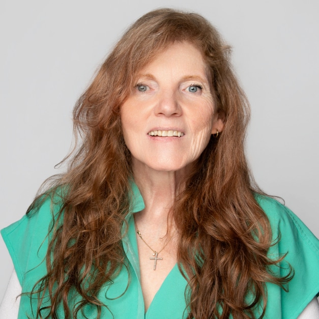 A woman with long brown hair wearing a green top and a cross necklace, smiling at the camera.