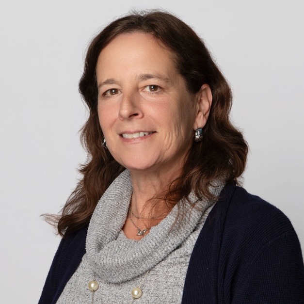 Smiling woman with shoulder-length brown hair, wearing a gray sweater and dark cardigan.