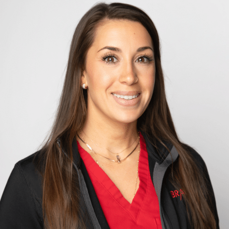 A smiling woman with long dark hair wearing a red top and black jacket.