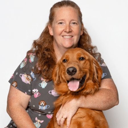 A smiling person with long hair hugging a happy golden retriever.